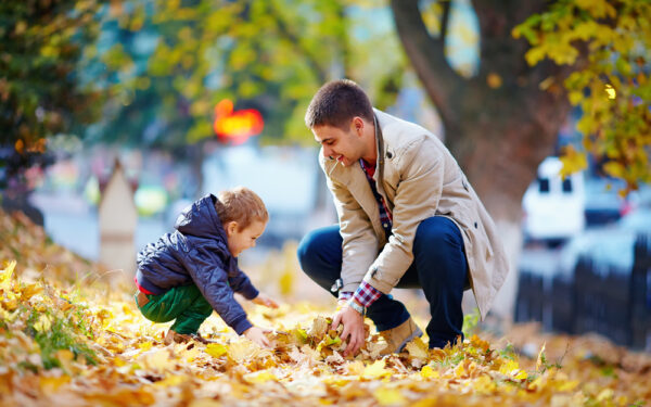 A man and boy playing in leaves on the ground.